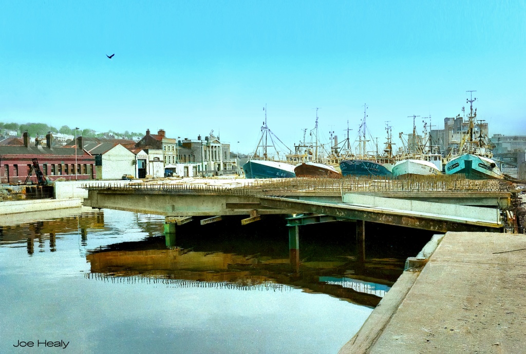 A partly constructed bridge in the foreground, with five trawlers just behind it. The River Lee runs under the bridge